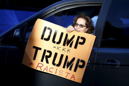 A woman holds a protest sign as she drives past the Luxe Hotel, where Republican presidential candidate Donald Trump was expected to speak in Brentwood, Los Angeles, California, United States July 10, 2015. REUTERS/Lucy Nicholson