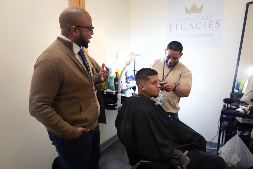 Ron Waddell, Founder and Executive Director of Legendary Legacies, left, talks with Jesus Pizarro, right, who is cutting the hair of Abrain Mendez, at his nonprofit organization, Friday, April 19, 2024, in Worcester, Mass. Waddell credits Blue Cross Blue Shield volunteers for truly investing in their employee service opportunities, which are increasing across the corporate realm. (AP Photo/Charles Krupa)