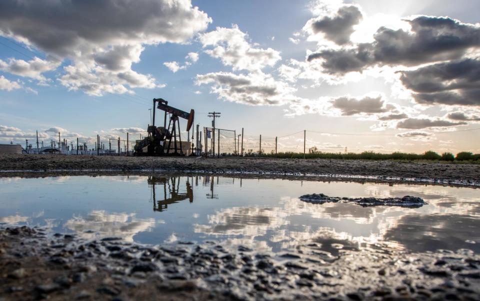 An oil pumpjack is reflected in a puddle of water.