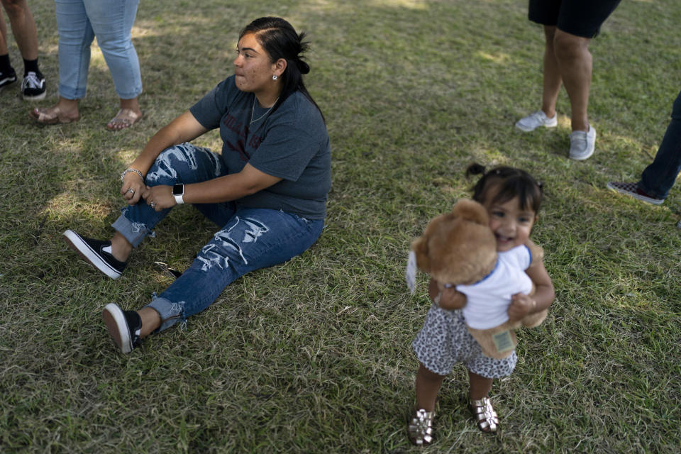 Jennifer Cantu, a kindergarten teacher visiting from Dilley, Texas, looks at a memorial honoring the victims killed in last week's school shooting in Uvalde, Texas, Friday, June 3, 2022, while her 1-year-old niece, Bryce Boswell, plays with a stuffed animal. It's hard to say exactly when some Texas educators began to feel like they were under siege, but the massacre of 19 students and two teachers at Robb Elementary School is only the latest, horrific episode in a string of events dating back years. (AP Photo/Jae C. Hong)