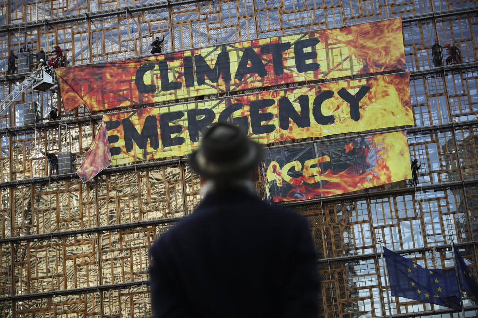 FILE - In this file photo dated Thursday, Dec. 12, 2019, a man looks up as police and fire personnel move in to remove climate activists and their banner, after they climbed the Europa building during a demonstration outside an EU summit meeting in Brussels. Massive challenges lay ahead for the European Union in 2020, as the impact of climate change seems likely to drive the bloc's thinking and policy initiatives over the coming years, starting Wednesday Jan. 1, 2020. (AP Photo/Francisco Seco, FILE)