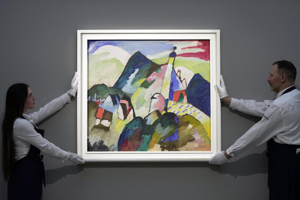 Members of staff hold the painting " Murnau with Church II" by Russian artist Wassily Kandinsky in 1910 is on display during a media preview of Sotheby's auction, in London, Wednesday, Feb. 22, 2023. The piece has an estimated price of 37 million pounds and will go on auction on March 1, 2023. (AP Photo/Kin Cheung)