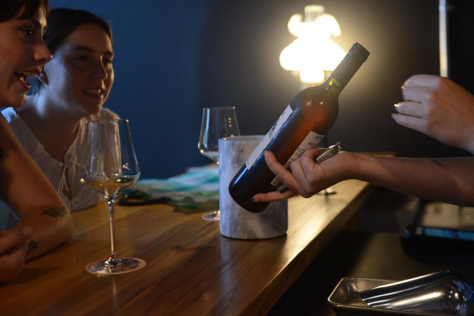 Bartender Hannah Bergmann (right) showing a wine bottle to guests during a private soft opening of Zero/Zero, a natural wine bar opening on June 9. Photo taken June 2, 2023.