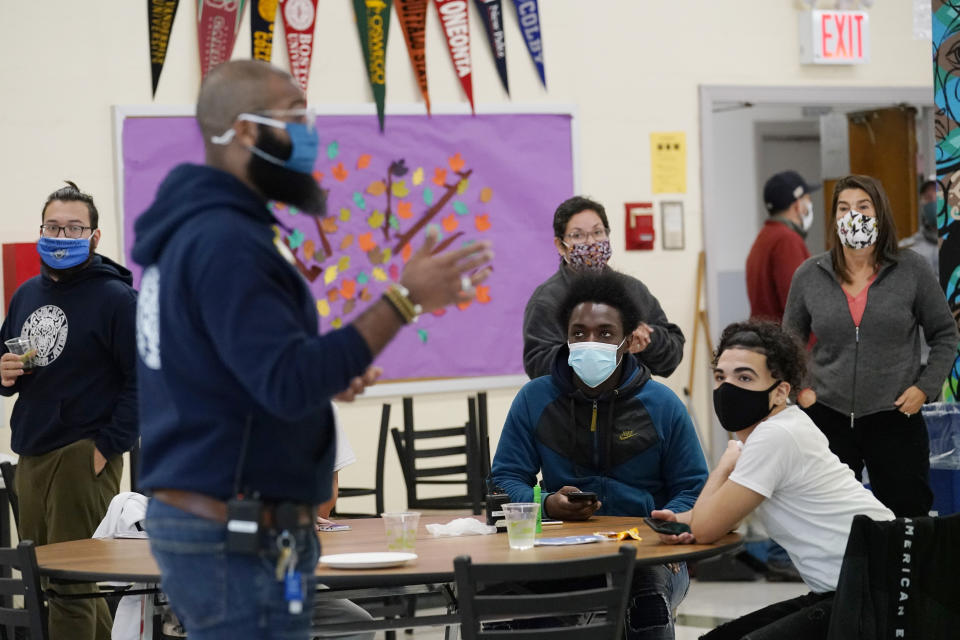 Students, teachers, administrators and counselors listen as principal Malik Lewis, foreground, second from left, teaches a history lesson during a pizza party and current events/trivia quiz in the cafeteria at West Brooklyn Community High School, Thursday, Oct. 29, 2020, in New York. The school is a "transfer school," catering to a students who haven't done well elsewhere, giving them a chance to graduate and succeed. (AP Photo/Kathy Willens)