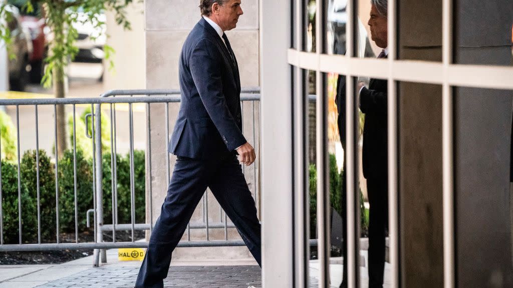 hunter biden walks into a building, he wears a dark suit with a white collared shirt and tie