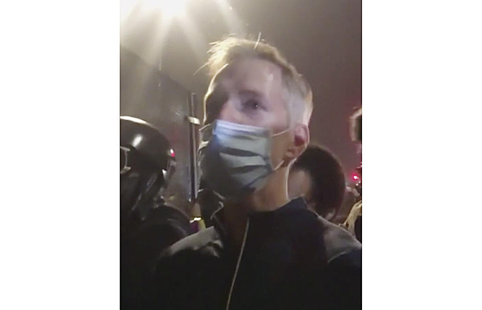 In this image made from video released by Karina Brown, Portland Mayor Ted Wheeler, stands at a fence guarding a federal courthouse as tear gas drifts by early July 23, 2020, in Portland Oregon, during another night of protest against the presence of federal agents sent by President Donald Trump to quell unrest in the city. (Karina Brown via AP)