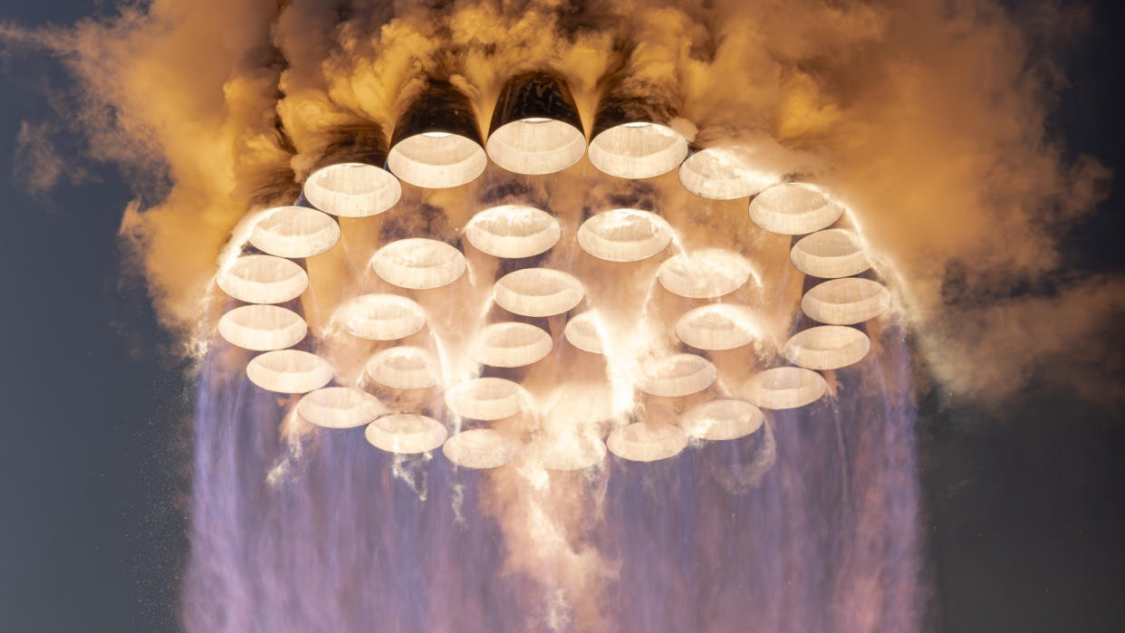  Close-up shot of 33 rocket engines burning, producing an orange glow and a blue-orange flame. 