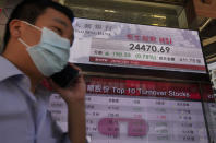 A man wearing face mask walks past a bank electronic board showing the Hong Kong share index at Hong Kong Stock Exchange Tuesday, April 28, 2020. Asian shares are mixed Tuesday as governments inch toward letting businesses reopen and central banks step in to provide cash to economies. (AP Photo/Vincent Yu)