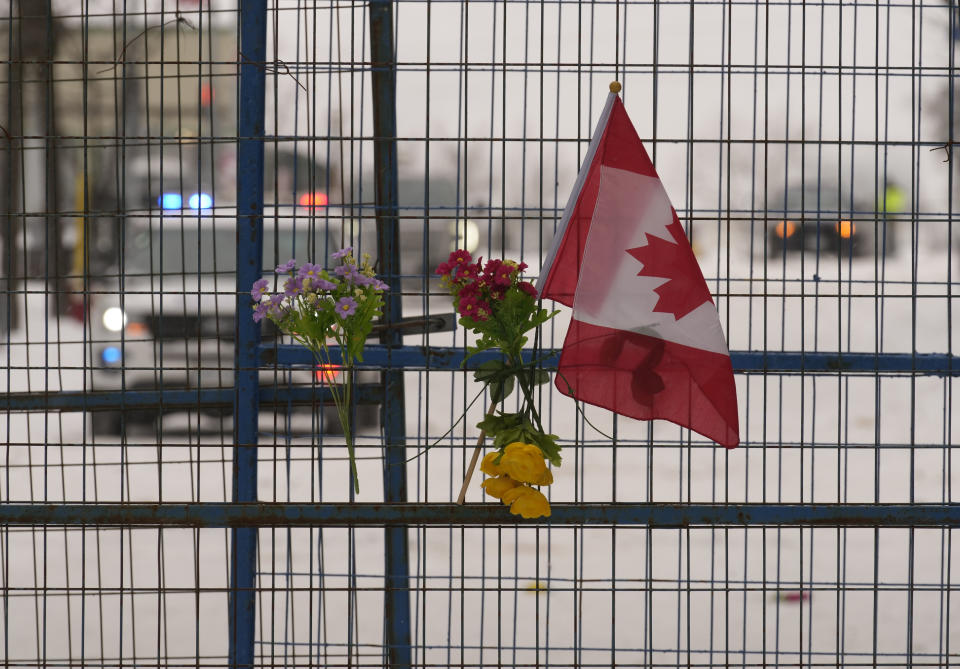 A small Canadian flag and flowers are shown on temporary fencing in downtown Ottawa on Sunday, Feb. 20, 2022. A protest, which was first aimed at a COVID-19 vaccine mandate for cross-border truckers but also encompassed fury over the range of COVID-19 restrictions. (Adrian Wyld/The Canadian Press via AP)