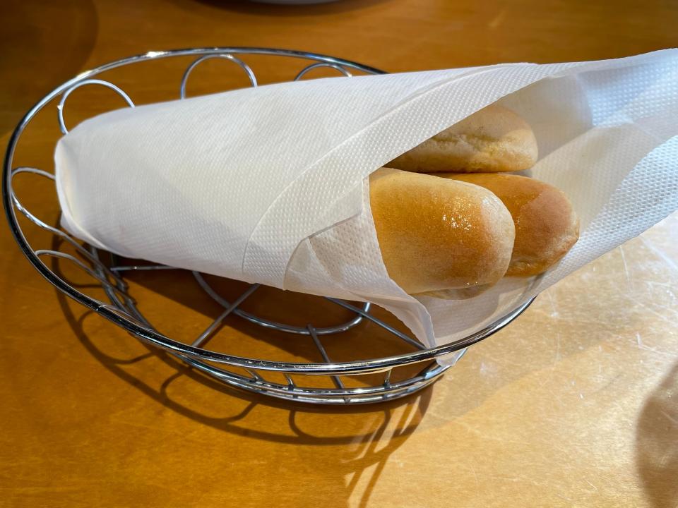 Metal basket of three breadsticks wrapped in paper on a brown table at Olive Garden