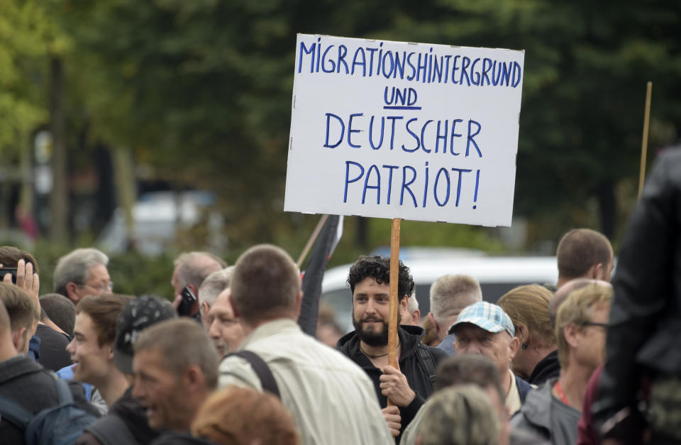 A protester holds a poster reading 'migration background and German patriot' in Chemnitz, eastern Germany, Saturday, Sept. 1, 2018, after several nationalist groups called for marches protesting the killing of a German man last week, allegedly by migrants from Syria and Iraq. (AP Photo/Jens Meyer)