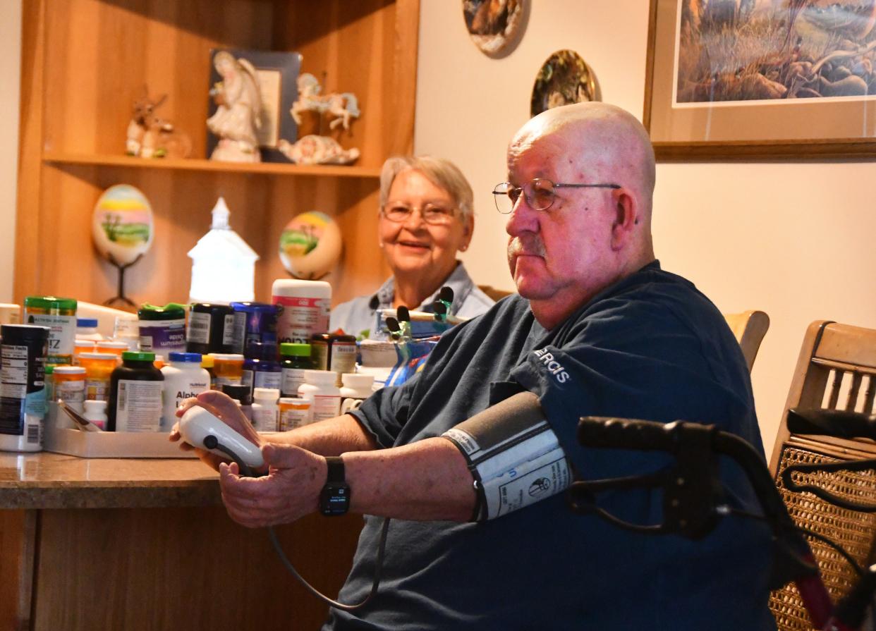 Daryl Wattenbarger, sitting at the dining room table with his wife, Kathy, checks his blood pressure. Daryl was in the hospital when he was offered a chance to participate in the Health First Hospital at Home program. The choice was obvious, he said: Stay in the hospital, or be at home with his dog and Kathy and her home-cooked meals. He was monitored by doctors and nurses in the teleremote monitoring program.