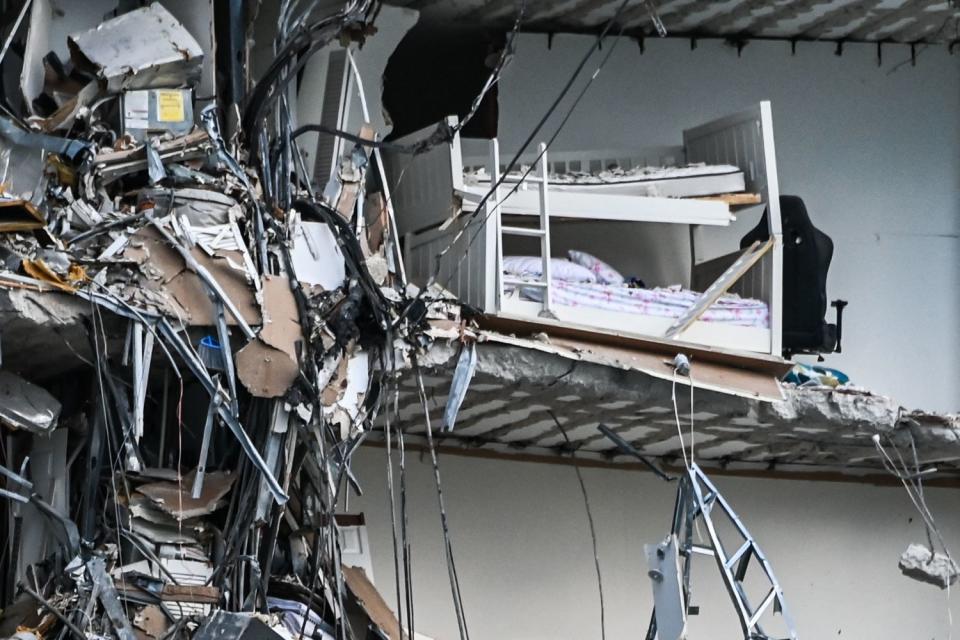 Shredded walls and wires hang beside a bunk bed and an office chair.