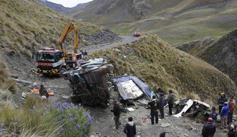 People stand around the remains of a bus that crashed in Inca Chaca on the outskirts of La Paz, Bolivia, Friday, Jan. 31, 2020. At least 14 people died and several were injured after the bus drove off a mountain road and fell down a ravine. (AP Photo/Juan Karita)