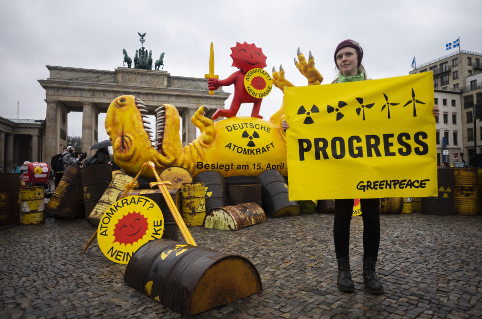 A Greenpeace activist poses with a poster in front of a mock-up dinosaur in front of the Brandenburg Gate during a rally marking the nuclear shutdown in Germany in Berlin, Germany, Saturday, April 15, 2023. Germany is shutting down its last three nuclear power plants on Saturday, April 15, 2023, as part of an energy transition agreed by successive governments. The signs read: 'Nuclear Power No Thanks' and the words on the dinosaur: 'German nuclear power defeated on April 15, 2023'. (AP Photo/Markus Schreiber)