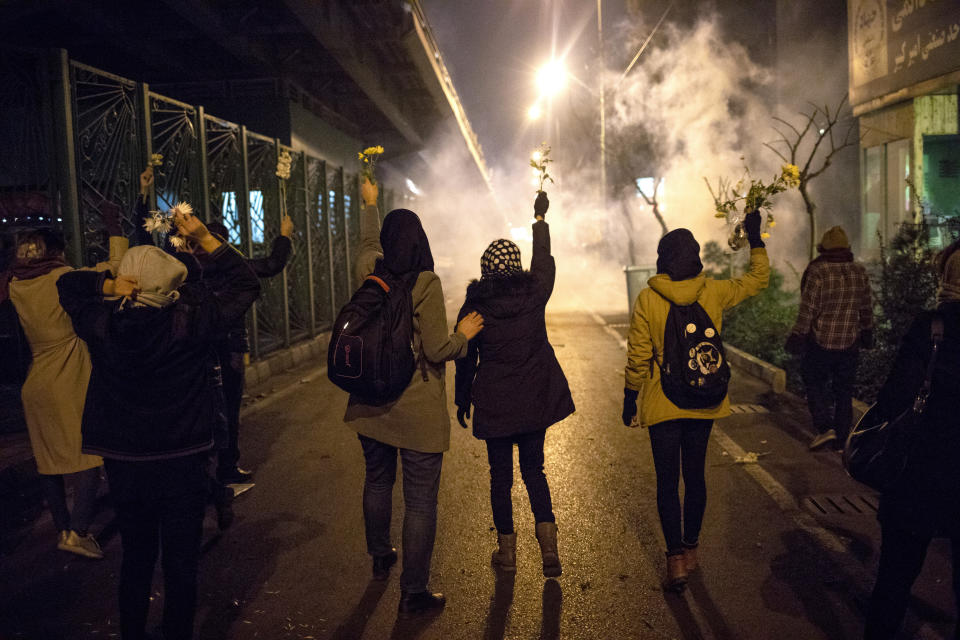 En esta imagen tomada el sábado 11 de enero de 2020, manifestantes alzan flores mientras se ve al fondo gas lacrimógeno lanzado por la policía, en una manifestación ante la Universidad Amir Kabir de Teherán, en Irán, en recuerdo por las víctimas de un avión ucraniano de pasajeros derribado por un misil iraní. (AP Foto)