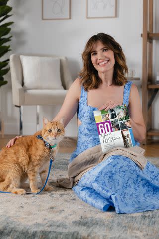 <p>Purina Cat Chow</p> Mandy Moore with a orange cat and Purina Cat Chow's '60 Years, 60 Stories: Celebrating the Extraordinary Impact of Cats' book