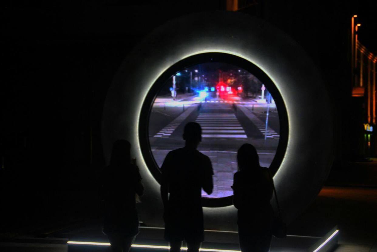 People looking through a portal between two cities.