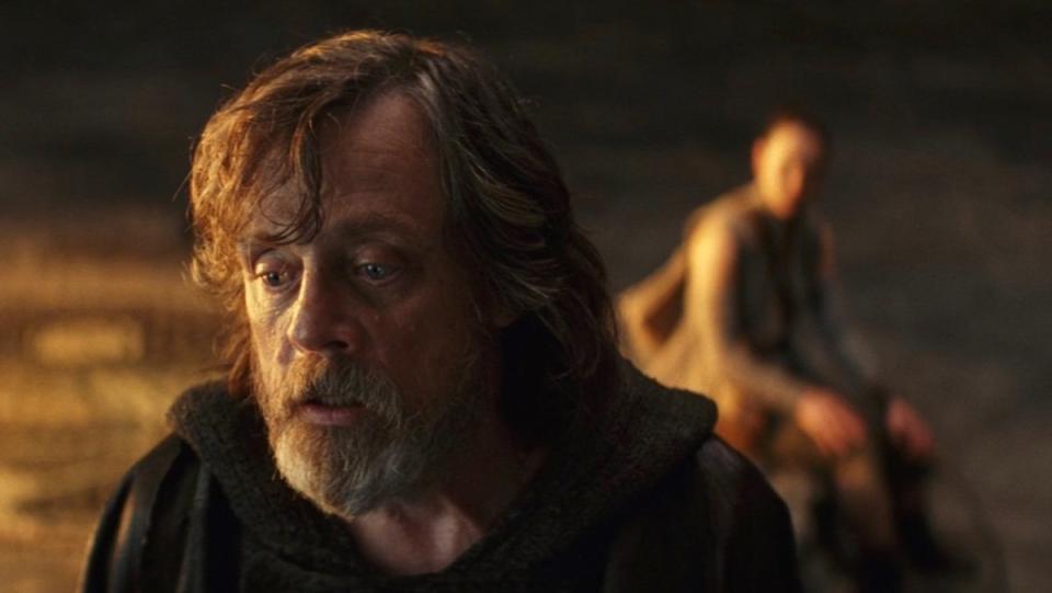 A sad and weary Luke Skywlaker in the forefront with Rey sitting behind him out of focus in The Last Jedi