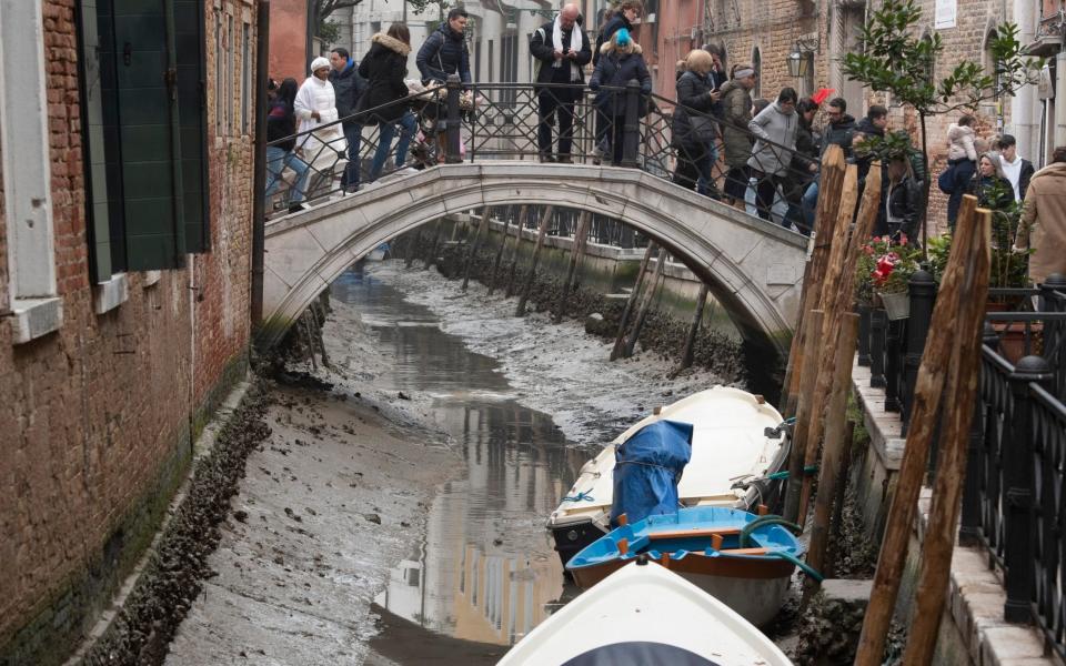 Boats are docked along a dried canal during a low tide in Venice, Italy - AP