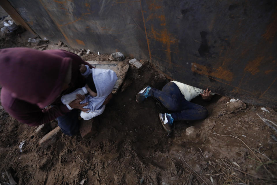 Honduran migrant Joel Mendez, 22, feeds his eight-month-old son Daniel as his partner Yesenia Martinez, 24, crawls through a hole under the U.S. border wall, in Tijuana, Mexico, Friday, Dec. 7, 2018. Moments later Martinez surrendered to waiting border guards while Mendez stayed behind in Tijuana to work, saying he feared he'd be deported if he crossed. (AP Photo/Rebecca Blackwell)