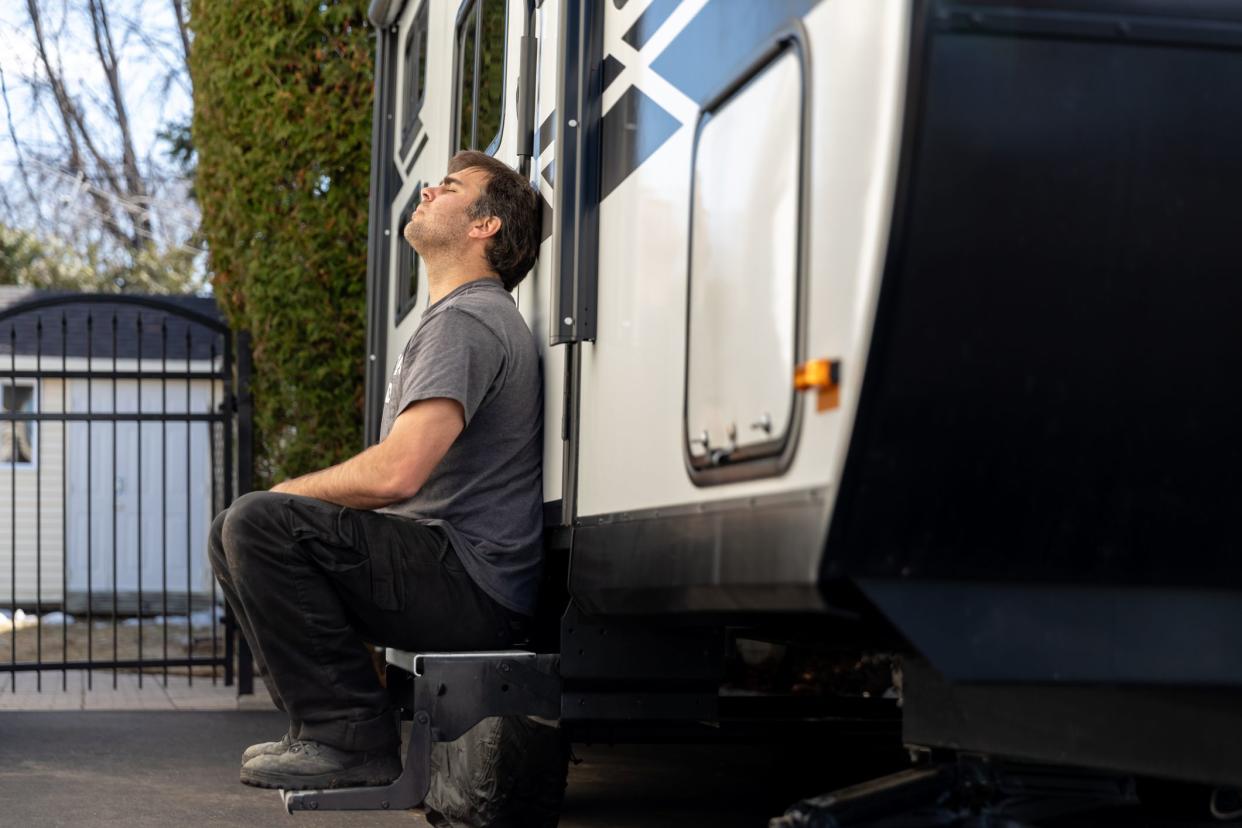 Man crying or being depressed after vacations are cancelled due to Covid-19 pandemic crisis. The woman is sitting on the steps of the travel trailer and feeling depressed.