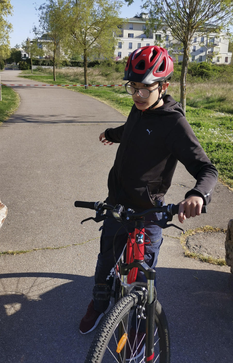 Mohammed, a 14-year-old with autism, on his bike outside his home Wednesday April 15, 2020 in Mantes-la-Jolie, west of Paris. France's confinement measures provide an exception for people with autism that allows them to go out in places where they are accustomed to. Coronavirus lockdown is proving an ordeal for kids with disabilities and their families who are having to care for them at home because special schools have been shut down to curb infections. (Courtesy of family via AP)