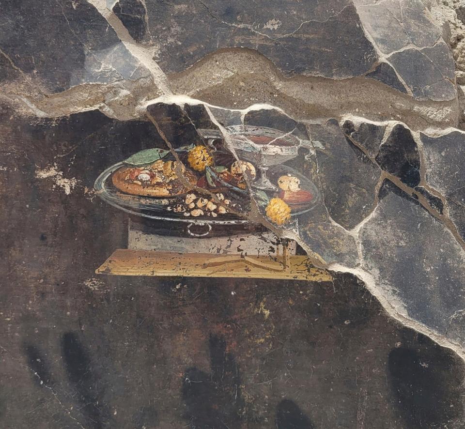 This picture provided on Tuesday, June 27, 2023, by the Pompeii Archaeological Park shows the wall of an ancient Pompeian house with a fresco depicting a table with food. The fresco was found in the atrium of a house in Insula 10 of Regio IX under excavation, to which a bakery was annexed, already partially explored between 1888 and 1891 and whose investigations were resumed last January. (Pompeii Archaeological Park via AP, ho)