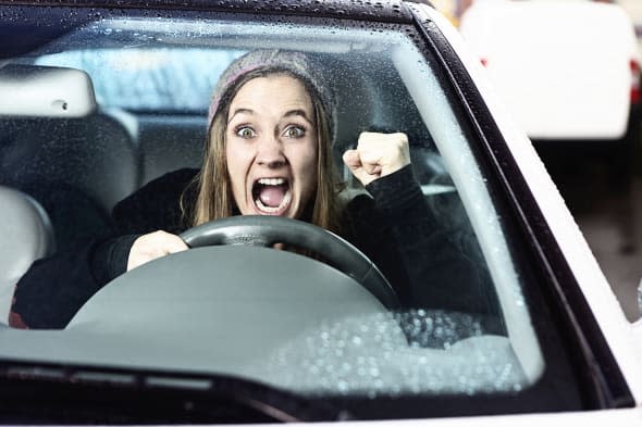 A furiously angry woman driving yells, shaking her fist through the windshield in a bout of road rage!