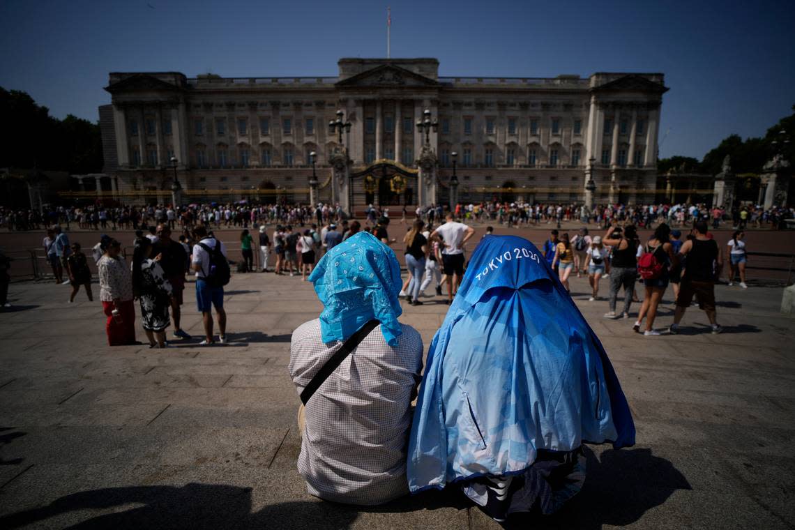 People sit covering their heads from the sun after a scaled down version of the Changing of the Guard ceremony took place outside Buckingham Palace, during hot weather in London, Monday, July 18, 2022. Britain’s first-ever extreme heat warning is in effect for large parts of England as hot, dry weather that has scorched mainland Europe for the past week moves north, disrupting travel, health care and schools. (AP Photo/Matt Dunham)