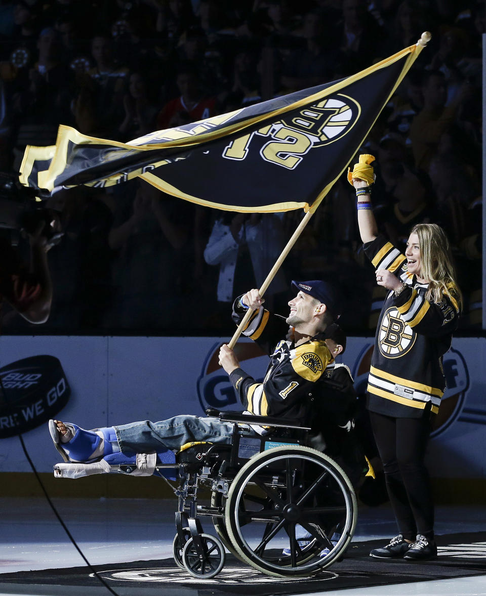 FILE - In this June 19, 2013 file photo, Boston Marathon bombing victim Marc Fucarile waves a "Boston Strong" flag with his fiancee, Jen Regan, and their son, Gavin, partially obscured, before Game 4 of the NHL hockey Stanley Cup Finals between the Boston Bruins and the Chicago Blackhawks in Boston. (AP Photo/Elise Amendola)