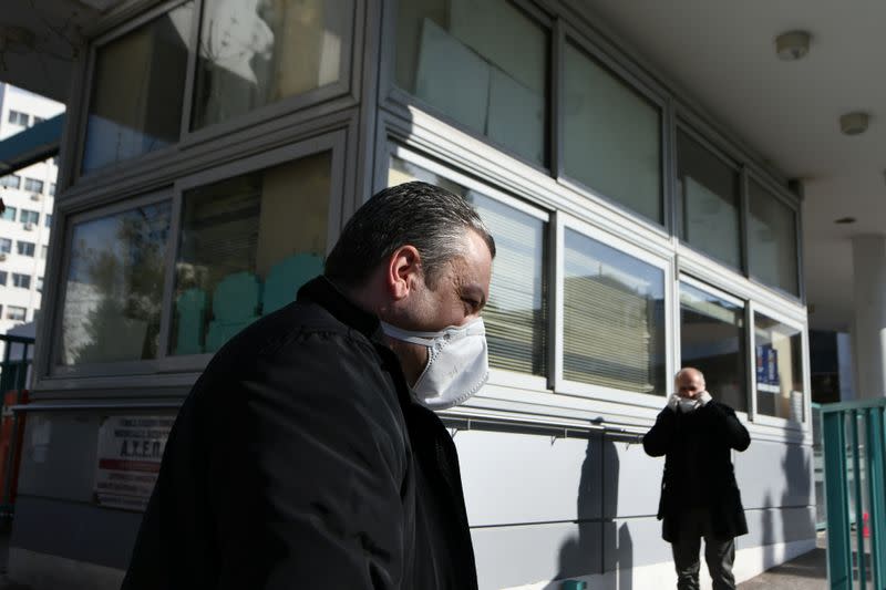 People wearing protective face masks sit outside the AHEPA hospital, where the first confirmed coronavirus case is being treated, in Thessaloniki