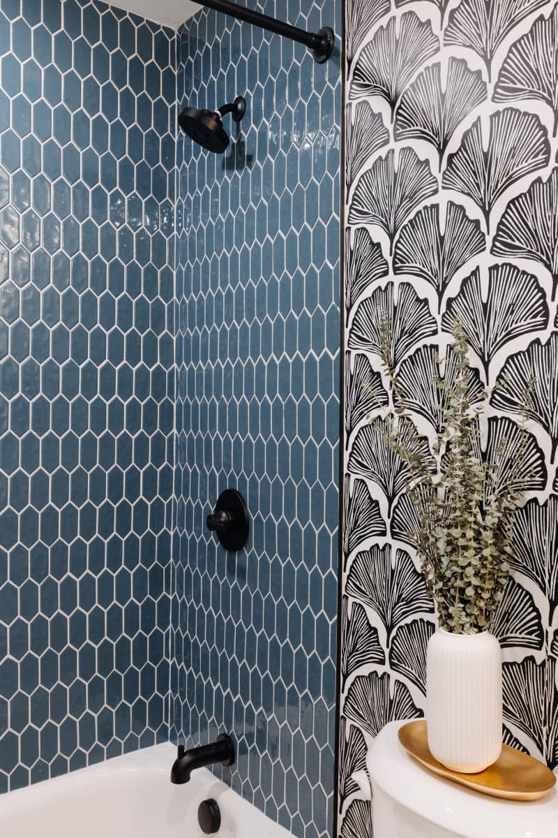 Bathroom with black and white gingko leaf print wallpaper and blue hexagonal tiled shower