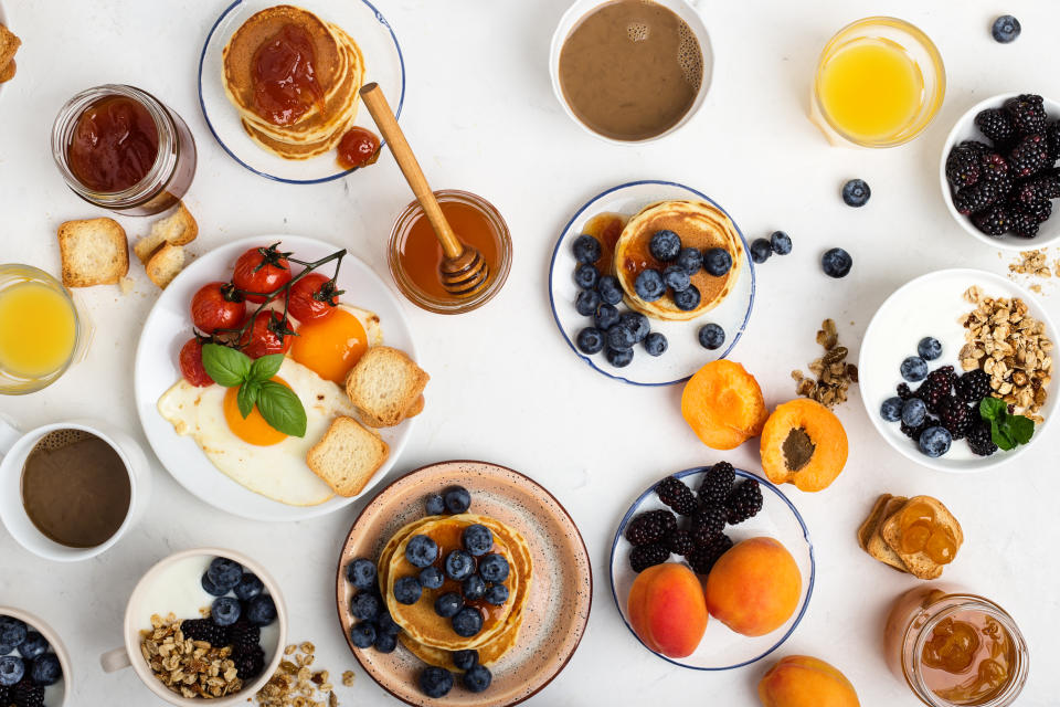 Healthy vegetarian breakfast or brunch, favorite meal. Homemade granola with yoghurt, pancakes, fried eggs, fresh summer fruits, berries, coffee and juice, honey on light gray table viewed from above