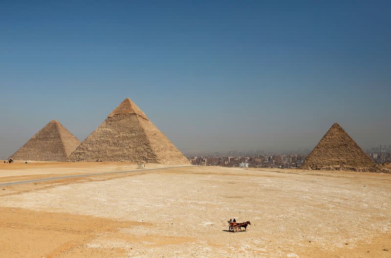 Tourists ride a horse-drawn cart in front of the Great Pyramids of Giza, on the outskirts of Cairo