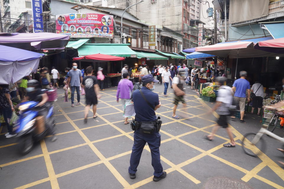 新冠肺炎疫情持續肆虐台灣，中央流行疫情指揮官陳時中呼籲，希望民眾在這週假日，盡量待在家並減少移動。不少民眾22日上午前往北投市場採購民生必需品，有員警在市場動線上維持秩序。
（中央社）  