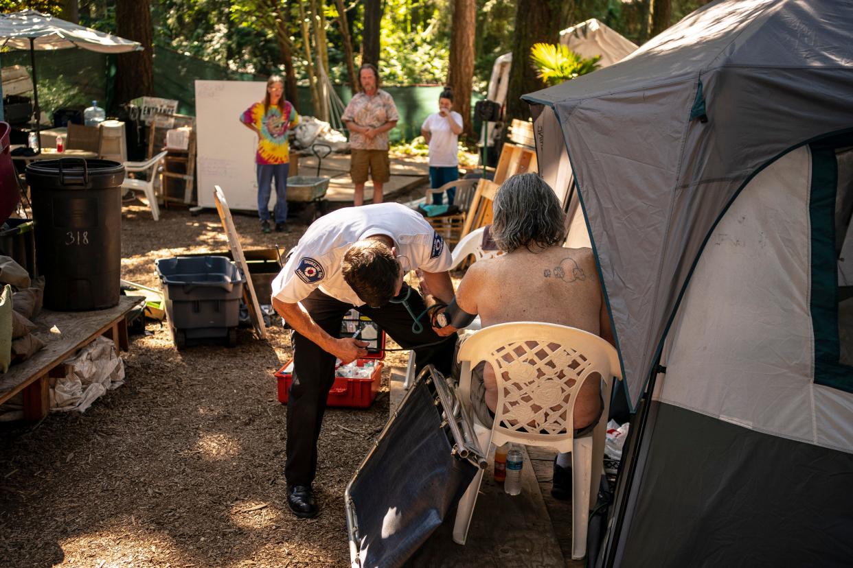 Gabe DeBay, Medical Services Officer with the Shoreline Fire Department, checks the blood pressure of a homeless man at a tent encampment during the hottest part of the day on July 26, 2022, in Shoreline, Washington. The Pacific Northwest is experiencing a heat wave with potentially record-breaking temperatures, which is expected to last for the rest of the week.