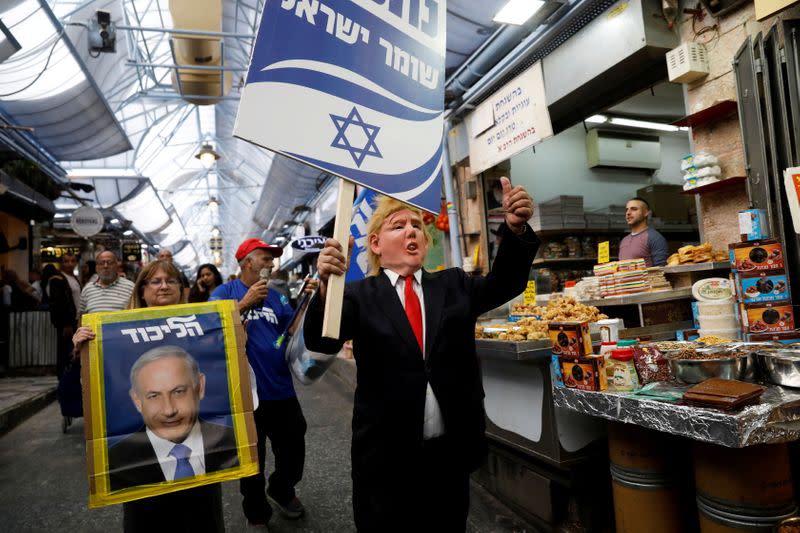 FILE PHOTO: Likud party supporters, one wearing a mask depicting U.S. President Donald Trump, hold election campaign placards, one depicting Israeli Prime Minister Benjamin Netanyahu, as they walk past stalls in Mahane Yehuda Market in Jerusalem