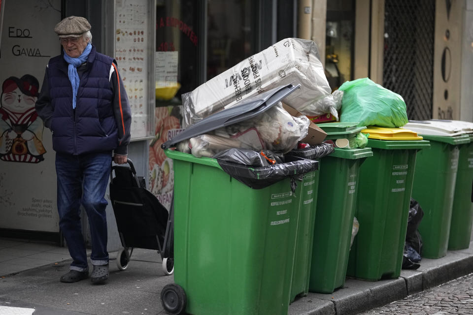 A man walks past not collected garbage cans, Thursday, March 9, 2023 in Paris. The show of anger against President Emmanuel Macron's plan to raise the retirement age from 62 to 64 is set to continue in coming days, as train and metro drivers, refinery workers, garbage collectors and others have said they would continue ongoing strikes. (AP Photo/Michel Euler)