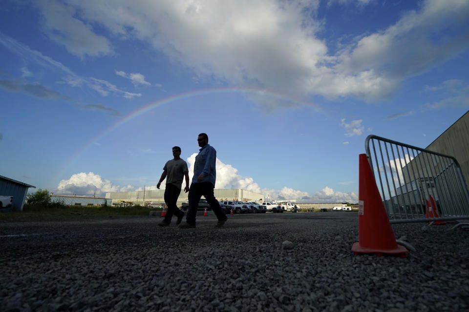 Josiah Goodman, left, and Austin Fleetwood, of Berryville, Ark. workers for Carroll Electric Cooperative Corporation, walk with a rainbow above them, through a tent city for electrical workers in Amelia, La., Thursday, Sept. 16, 2021. When Hurricane Ida was brewing in the Gulf of Mexico, the grass was chest high and the warehouse empty at this lot in southeastern Louisiana. Within days, electric officials transformed it into a bustling “tent city” with enormous, air-conditioned tents for workers, a gravel parking lot for bucket trucks and a station to resupply crews restoring power to the region. (AP Photo/Gerald Herbert)