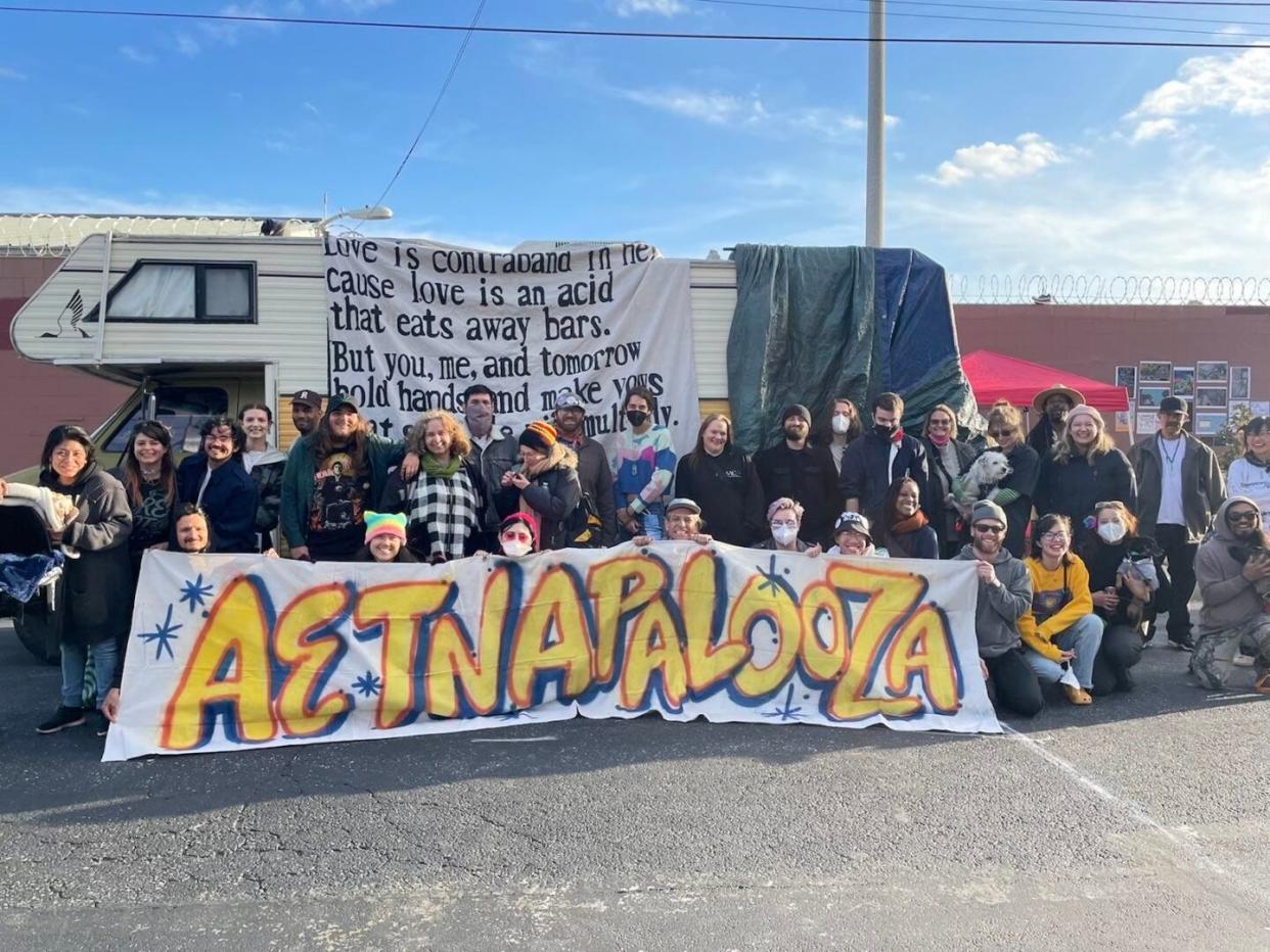 Carla Orendorff and organizers with Aetna Street Solidarity stand with a banner celebrating Aetnapalooza, a street fair for unhoused people, on April 22, 2023.