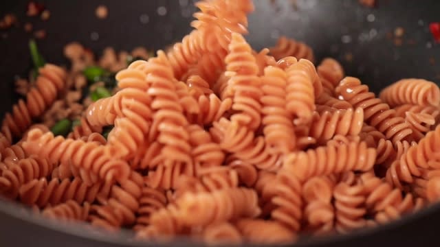 Adding cooked red lentil pasta to frying pan