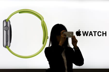 A woman takes pictures with a smart phone as she stands in front of an Apple Watch display at an electronics store in Omotasando in Tokyo April 24, 2015. REUTERS/Thomas Peter