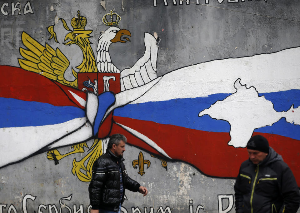 People walk by the graffiti that shows Serbian, left, and Russian flags with maps of Kosovo and Crimea in northern, Serb-dominated part of ethnically divided town of Mitrovica, Kosovo, Saturday, Dec. 15, 2018. Serbia threatened a possible armed intervention in Kosovo after the Kosovo parliament on Friday overwhelmingly approved the formation of a regular army, and Russia denounced the move. (AP Photo/Darko Vojinovic)