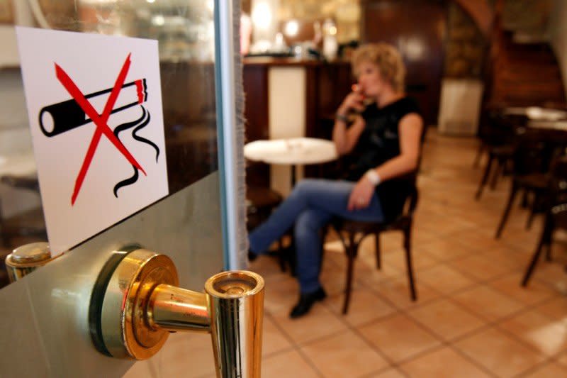 A woman smokes a cigarette behind a smoking ban sign in a restaurant-cafe in central Athens October 18, 2010.  REUTERS/John Kolesidis