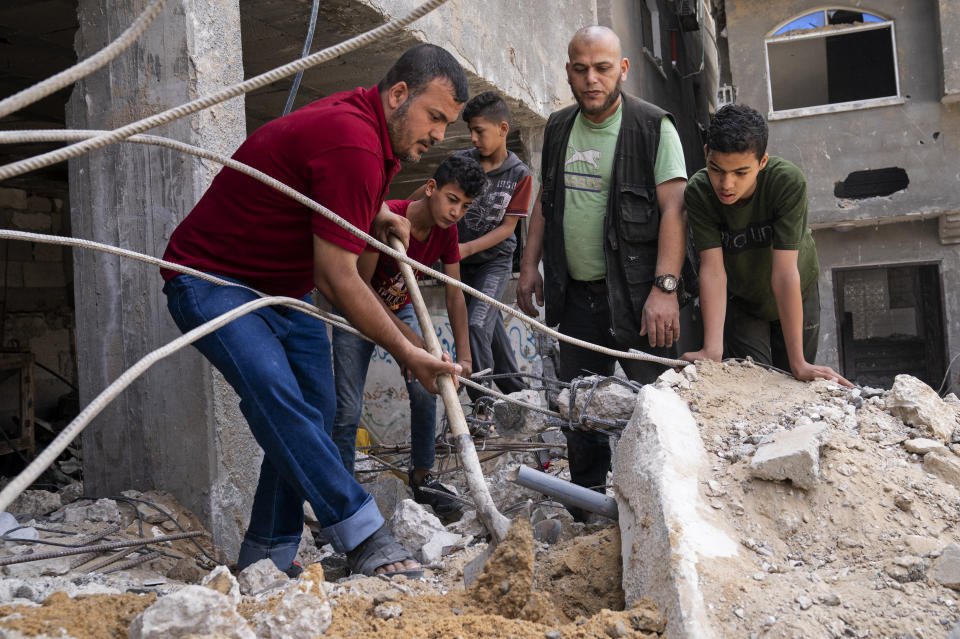 Ramez al-Masri, 39, left, uses a shovel to dig under a block of concrete beside the crater where his home was destroyed by an air-strike prior to a cease-fire reached after an 11-day war between Gaza's Hamas rulers and Israel, Sunday, May 23, 2021, in Beit Hanoun, the northern Gaza Strip. (AP Photo/John Minchillo)