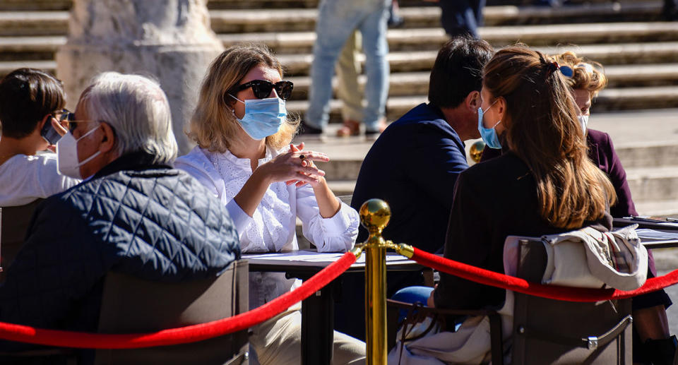 Two women wearing face masks sit chatting at a table in Italy.