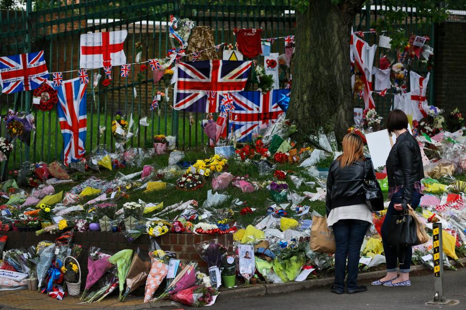 People look at some of the thousands of floral and other tributes left in honour of murdered 25-year-old British soldier Lee Rigby, at the scene near Woolwich Barracks in London, Wednesday, May 29, 2013. Two men attacked and killed the off-duty soldier in broad daylight, Wednesday, May 22. They were shot by police and arrested on suspicion of murder. (AP Photo/Lefteris Pitarakis)