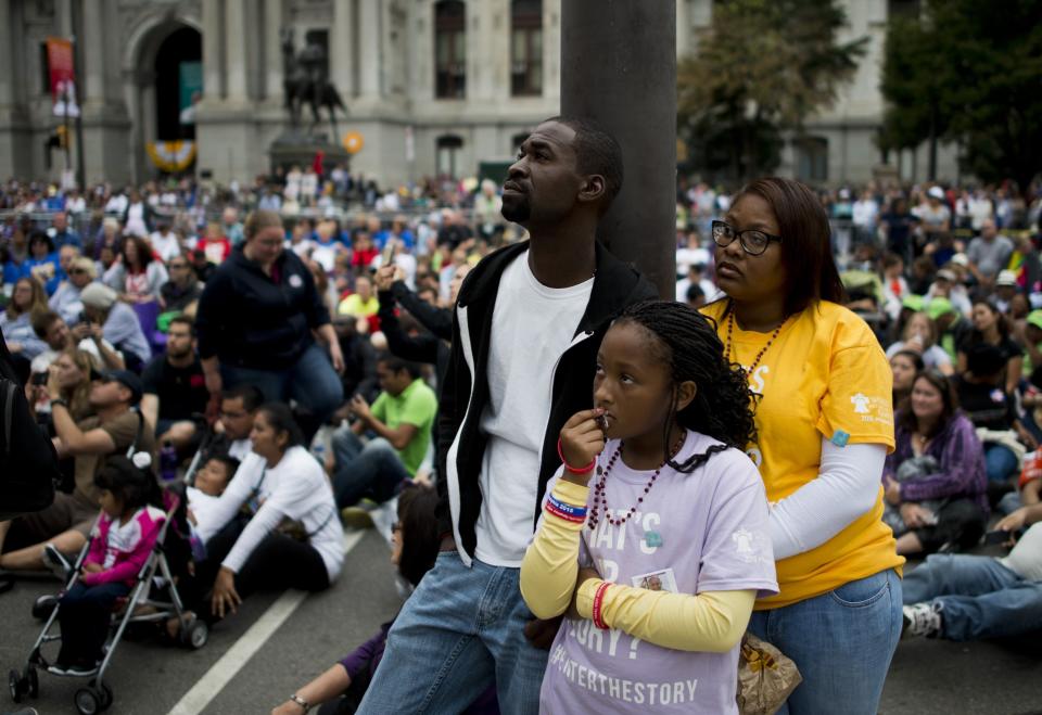 A family watches a Mass on a large screen with Pope Francis in downtown Philadelphia.