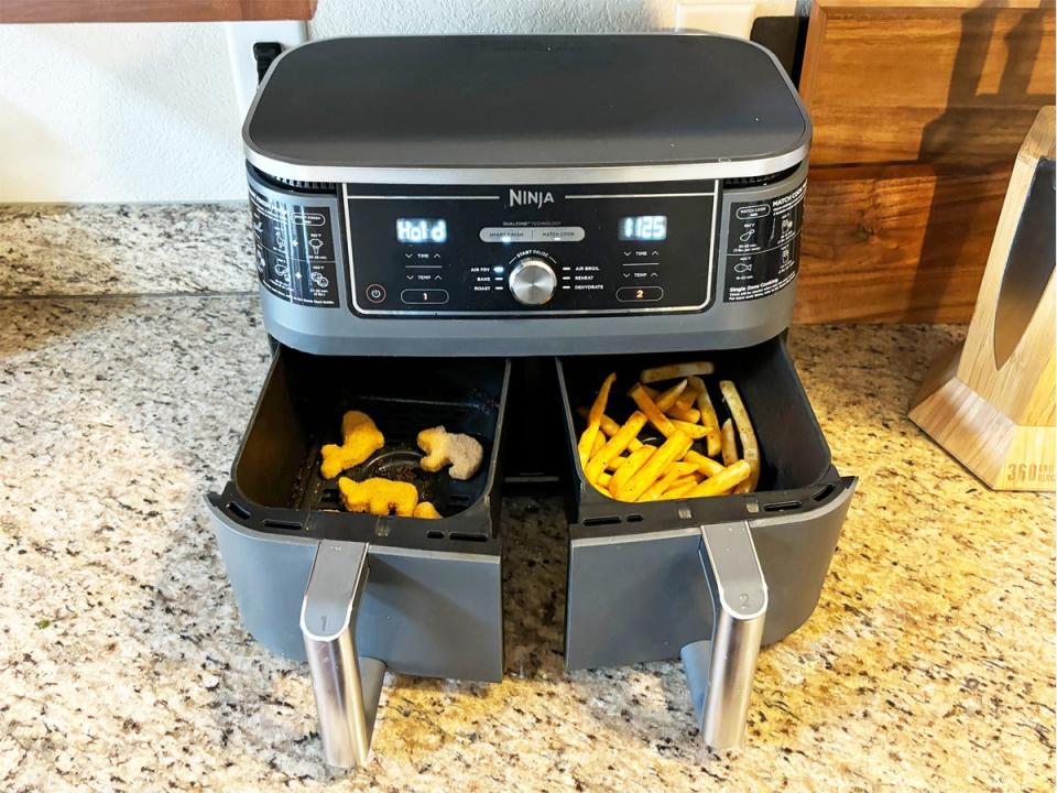 Ninja Foodi DualZone Air Fryer with both baskets opened showing chicken nuggets in one and fries in the other.